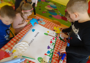 Dzieci dekorują plakat, wycinają, naklejają kolorowe elementy z papieru.